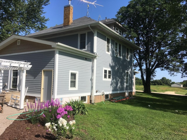 back of house featuring a chimney, a lawn, and a pergola