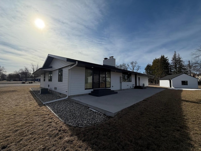 view of front facade featuring an outbuilding, a front lawn, a patio, central AC unit, and a chimney