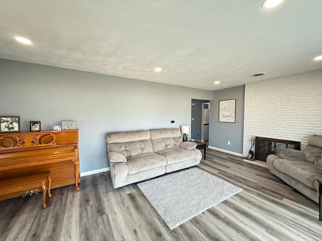 living area with visible vents, a brick fireplace, baseboards, and wood finished floors