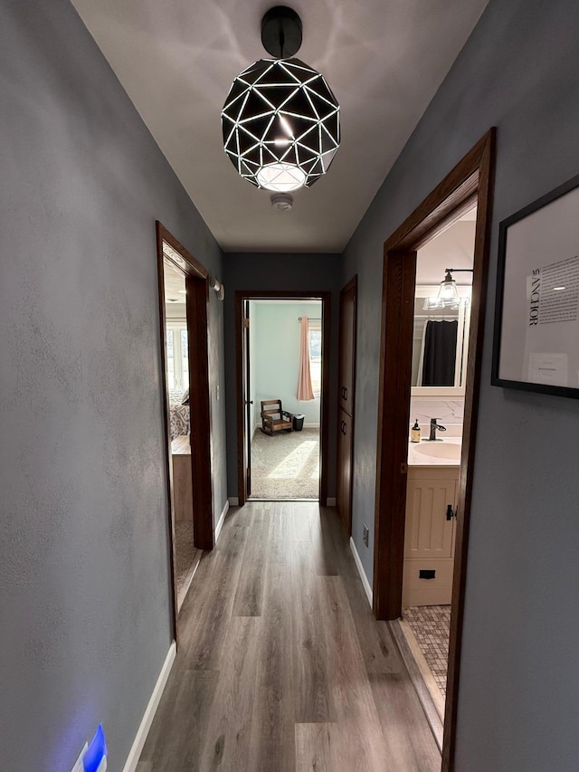 hall with wood finished floors, baseboards, and a sink