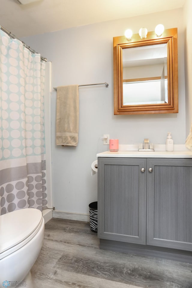 full bath featuring toilet, curtained shower, wood finished floors, baseboards, and vanity