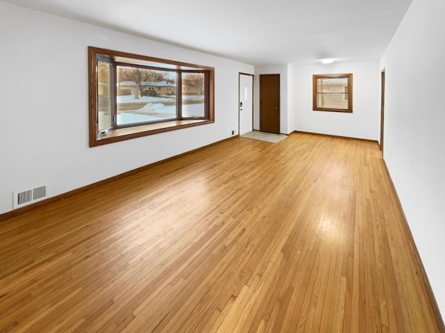 spare room with light wood-type flooring, visible vents, and baseboards