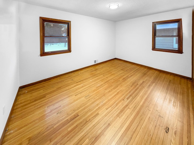 spare room featuring visible vents, light wood-style floors, baseboards, and a textured ceiling