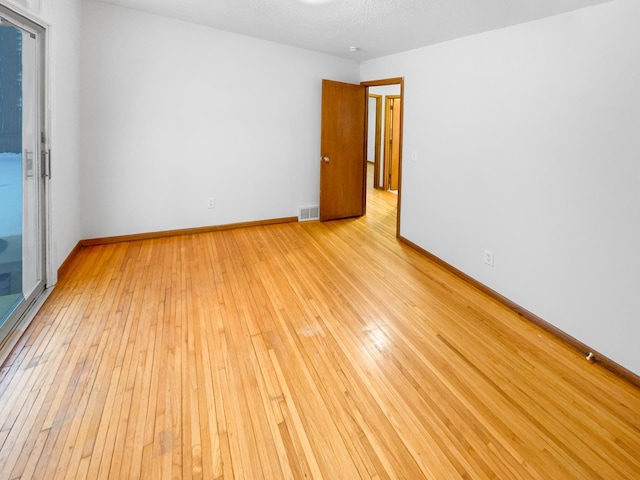 unfurnished room with baseboards, visible vents, light wood finished floors, and a textured ceiling