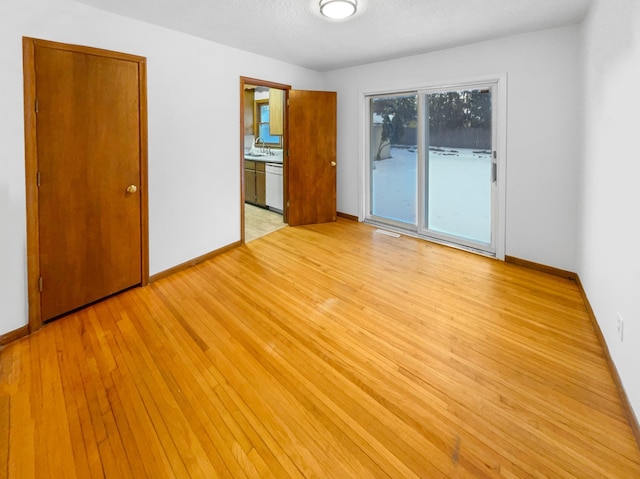 unfurnished bedroom featuring a sink, baseboards, light wood-style flooring, and access to outside