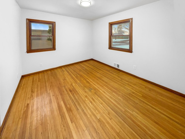 unfurnished room with a wealth of natural light, visible vents, light wood-style flooring, and baseboards