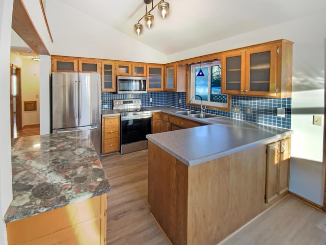 kitchen featuring light wood-type flooring, lofted ceiling, a peninsula, stainless steel appliances, and a sink