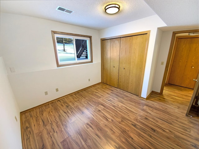 unfurnished bedroom with visible vents, baseboards, wood finished floors, a closet, and a textured ceiling