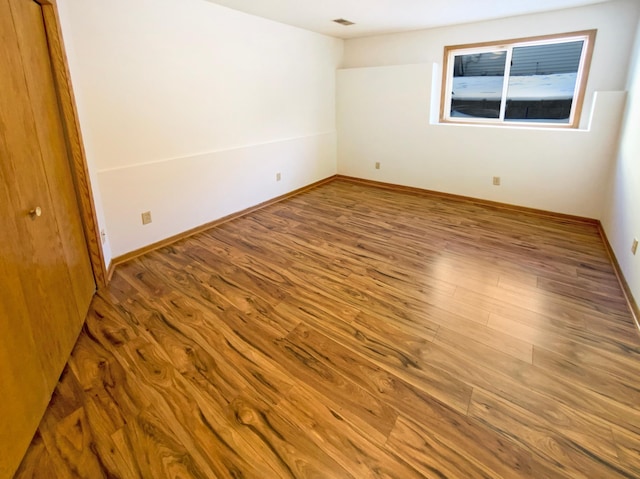 unfurnished room featuring wood finished floors, visible vents, and baseboards