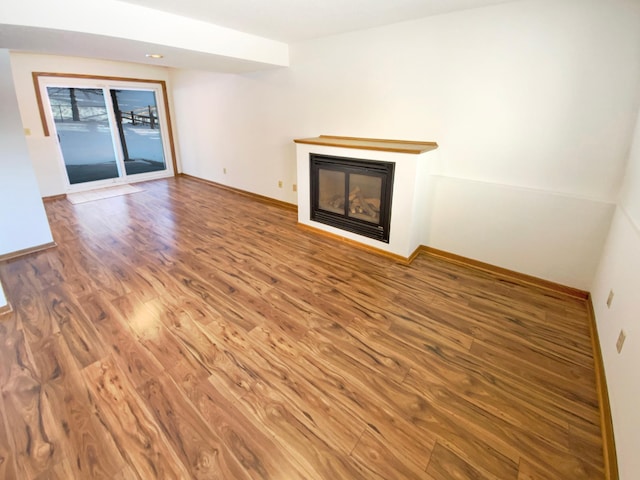 unfurnished living room with a glass covered fireplace, baseboards, and wood finished floors