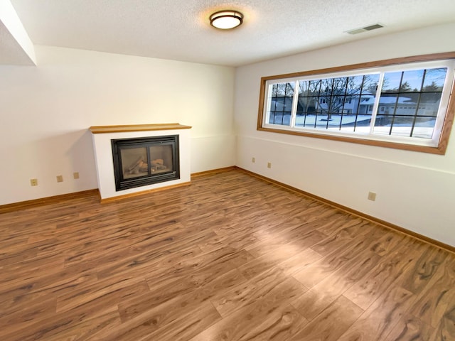 unfurnished living room with wood finished floors, baseboards, visible vents, a textured ceiling, and a glass covered fireplace