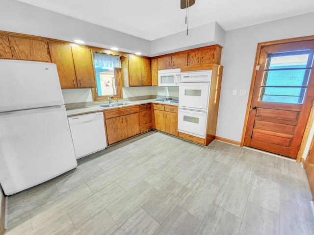 kitchen featuring brown cabinets, a sink, white appliances, light countertops, and baseboards