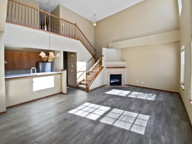 unfurnished living room featuring a chandelier, stairway, a high ceiling, and wood finished floors