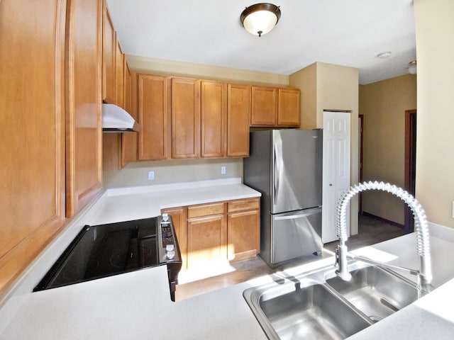 kitchen featuring a sink, under cabinet range hood, freestanding refrigerator, stovetop, and light countertops