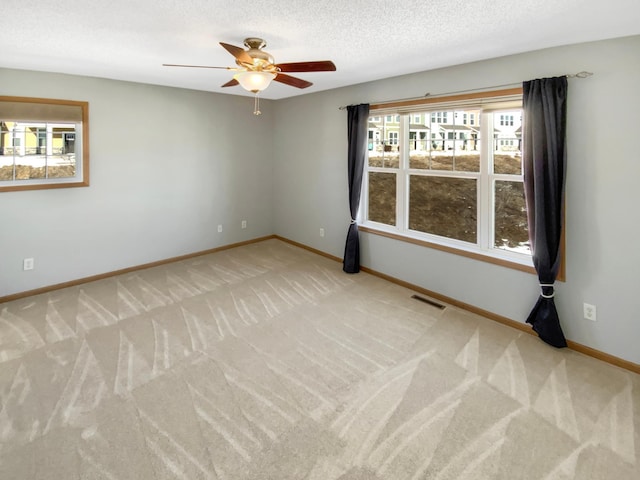 spare room featuring a ceiling fan, baseboards, carpet, visible vents, and a textured ceiling