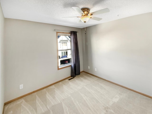 spare room featuring light carpet, ceiling fan, a textured ceiling, and baseboards