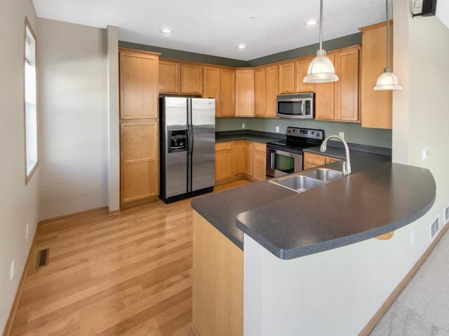 kitchen featuring visible vents, a peninsula, a sink, appliances with stainless steel finishes, and dark countertops