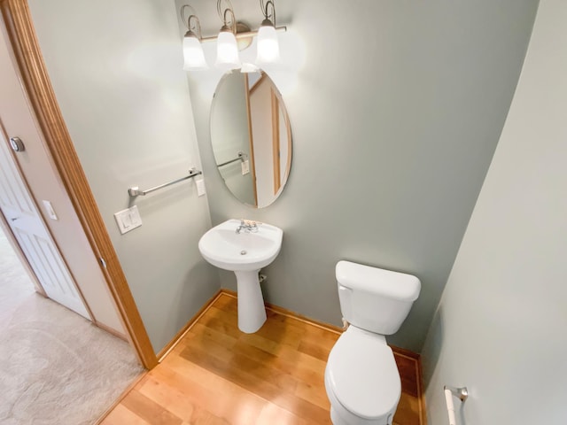 half bathroom with toilet, wood finished floors, and baseboards