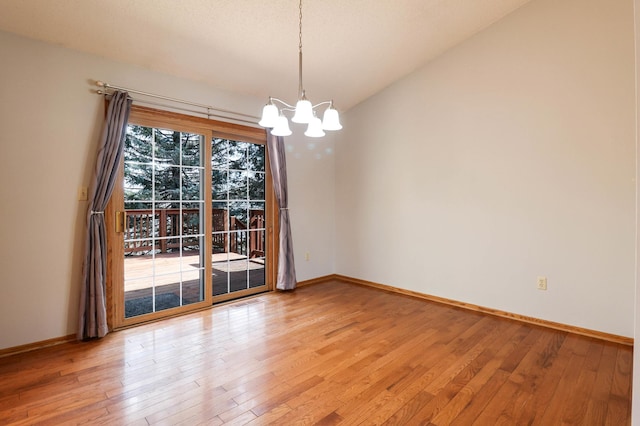 spare room featuring an inviting chandelier, baseboards, and light wood-style floors