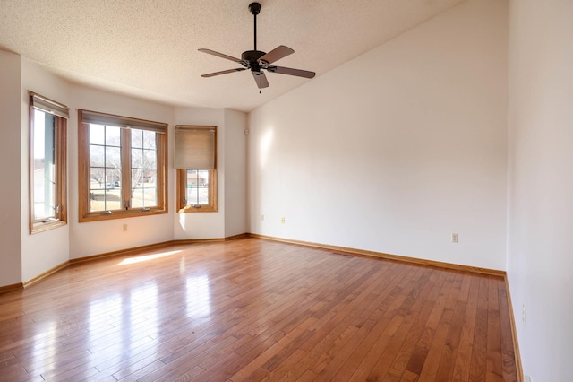 unfurnished room with vaulted ceiling, a textured ceiling, baseboards, and wood-type flooring