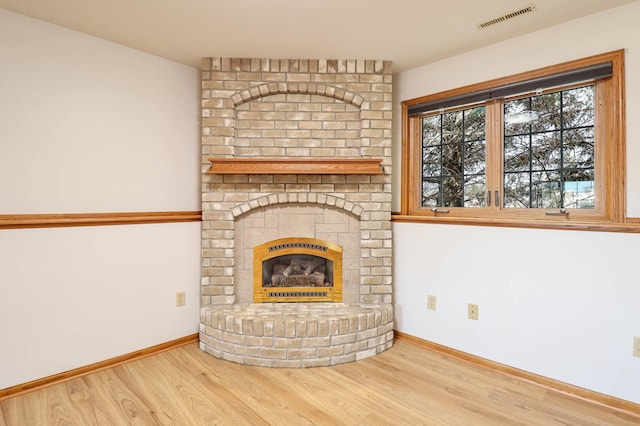 unfurnished living room with wood finished floors, a fireplace, visible vents, and baseboards