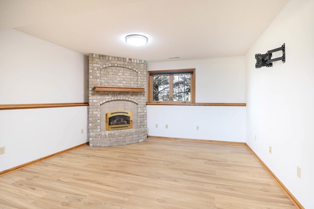 unfurnished living room with baseboards, a brick fireplace, and wood finished floors