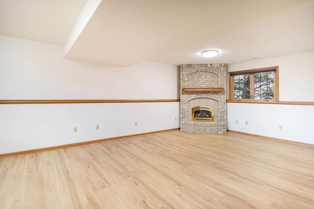 unfurnished living room with baseboards, a brick fireplace, and wood finished floors