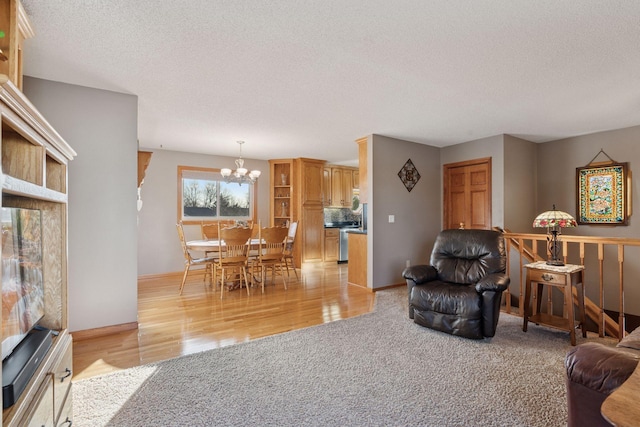 living area with a textured ceiling, baseboards, an inviting chandelier, light carpet, and light wood-type flooring