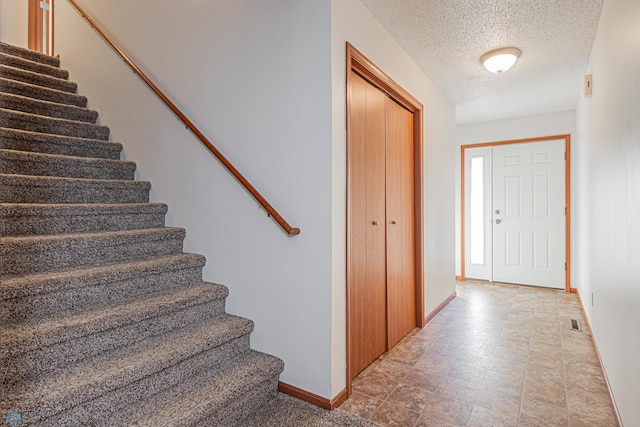 entryway with visible vents, stairway, a textured ceiling, and baseboards