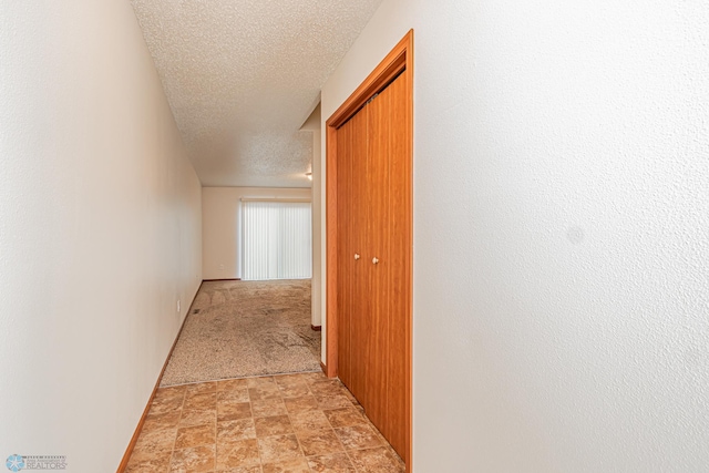 hallway with a textured ceiling, stone finish flooring, and baseboards