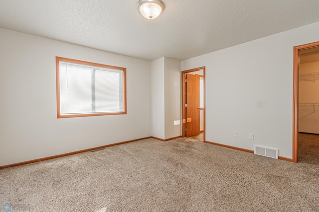 carpeted spare room featuring visible vents, a textured ceiling, and baseboards