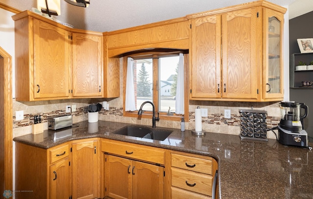 kitchen with a sink, dark stone counters, glass insert cabinets, and decorative backsplash