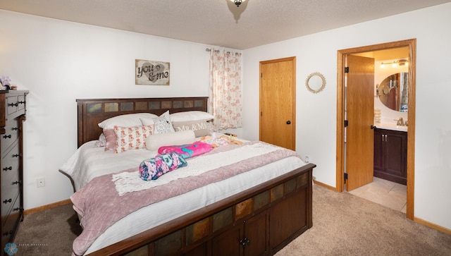 bedroom featuring baseboards, light colored carpet, a textured ceiling, ensuite bath, and a sink