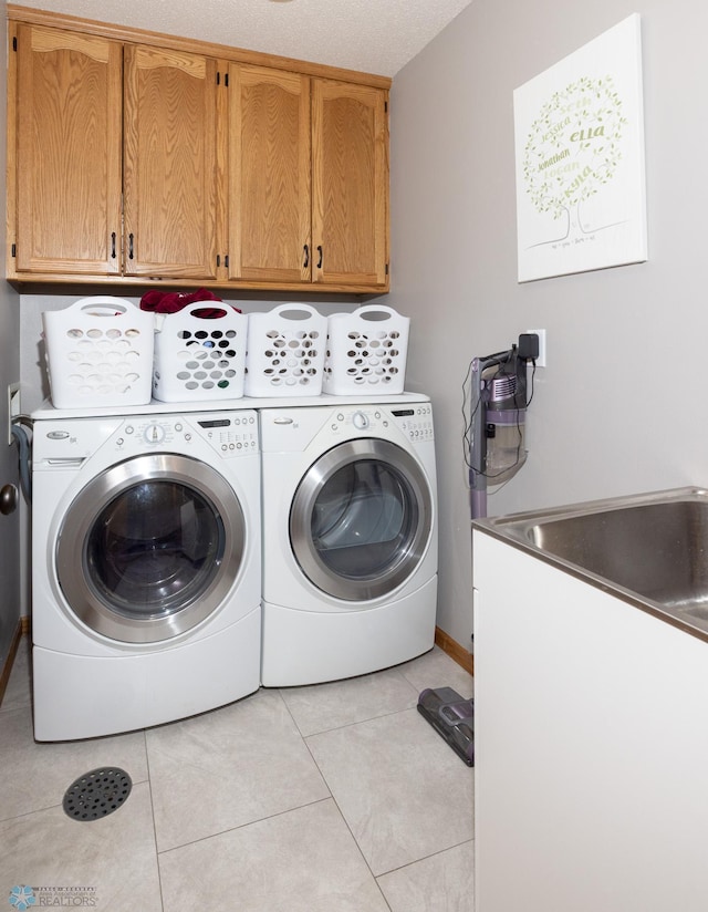 clothes washing area featuring washer and clothes dryer, light tile patterned floors, and cabinet space