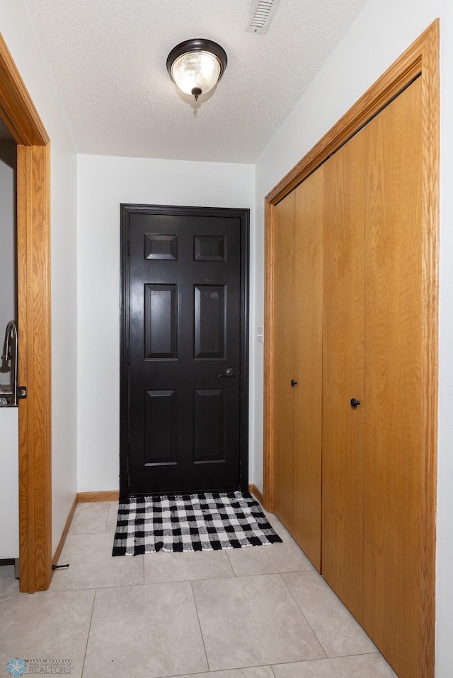 foyer entrance featuring light tile patterned floors, baseboards, visible vents, and a textured ceiling