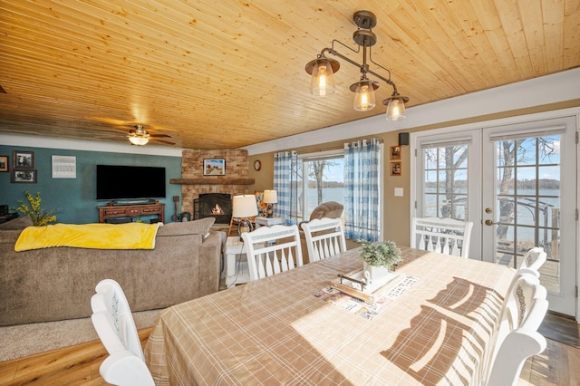 dining area with wood finished floors, french doors, a stone fireplace, wooden ceiling, and ceiling fan