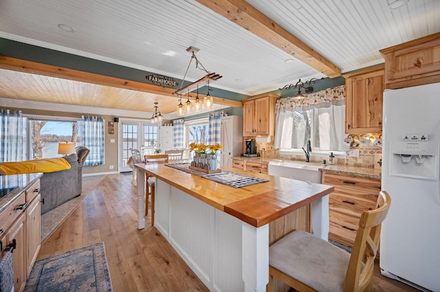 kitchen with beamed ceiling, a kitchen bar, a sink, white fridge with ice dispenser, and butcher block counters