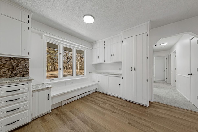 kitchen with a baseboard heating unit, backsplash, white cabinetry, and light wood finished floors