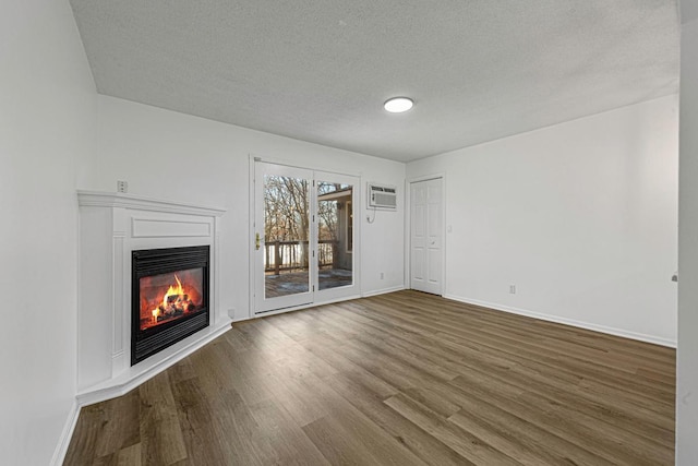 unfurnished living room featuring wood finished floors, baseboards, a wall mounted AC, a textured ceiling, and a glass covered fireplace