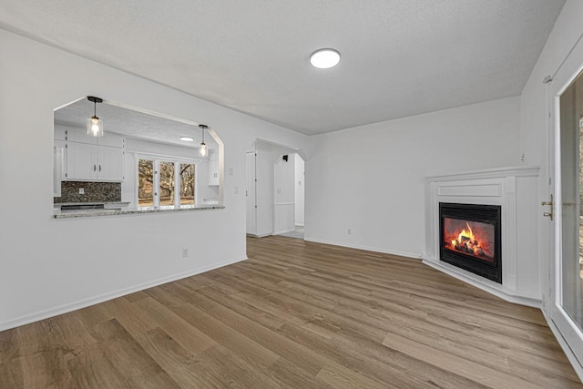 unfurnished living room with a glass covered fireplace, baseboards, arched walkways, and wood finished floors