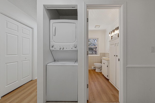 clothes washing area with laundry area, wainscoting, stacked washer and clothes dryer, and light wood-style floors