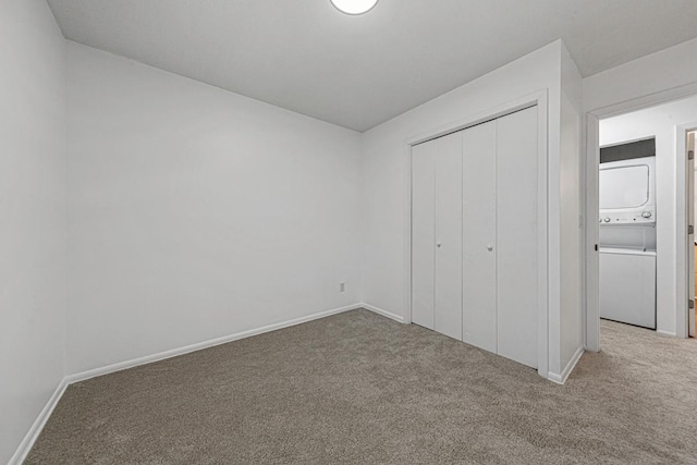 unfurnished bedroom featuring carpet flooring, baseboards, stacked washer / drying machine, and a closet