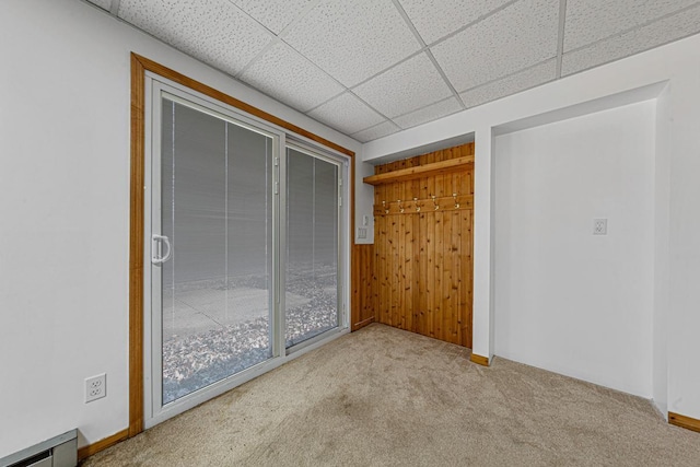 unfurnished bedroom featuring carpet flooring, a paneled ceiling, wood walls, and a baseboard radiator