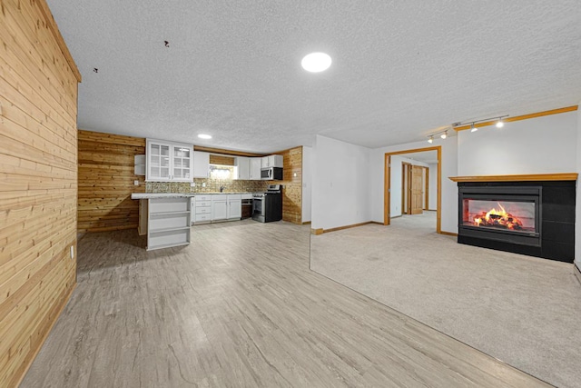 unfurnished living room featuring wooden walls, a multi sided fireplace, track lighting, a textured ceiling, and light wood-type flooring