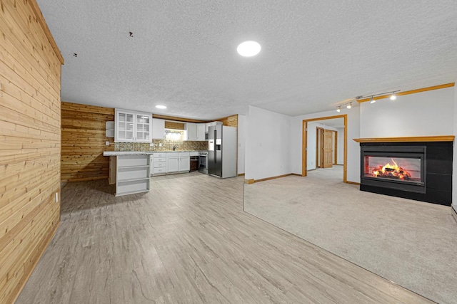 unfurnished living room featuring a textured ceiling, light wood-style floors, wooden walls, rail lighting, and a multi sided fireplace