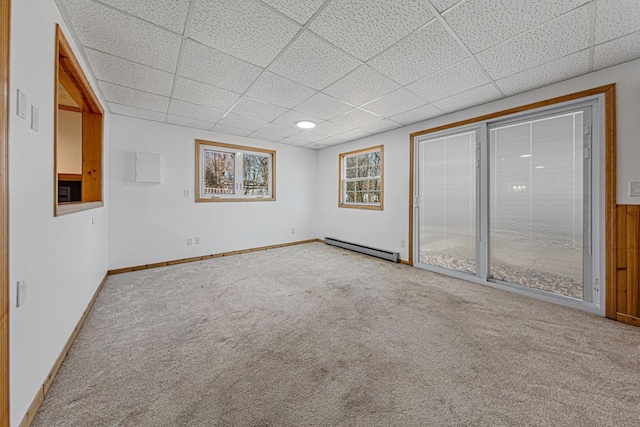 carpeted spare room featuring a drop ceiling, baseboards, and a baseboard radiator