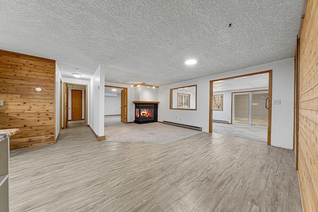 unfurnished living room with wood finished floors, a baseboard radiator, wood walls, a glass covered fireplace, and baseboard heating