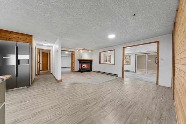 unfurnished living room featuring light wood finished floors, a glass covered fireplace, a textured ceiling, and a baseboard heating unit