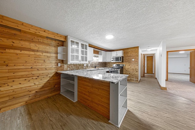 kitchen with light stone counters, open shelves, a peninsula, white cabinets, and appliances with stainless steel finishes