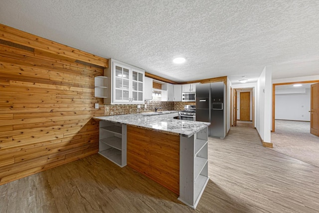 kitchen featuring open shelves, light stone counters, appliances with stainless steel finishes, a peninsula, and glass insert cabinets